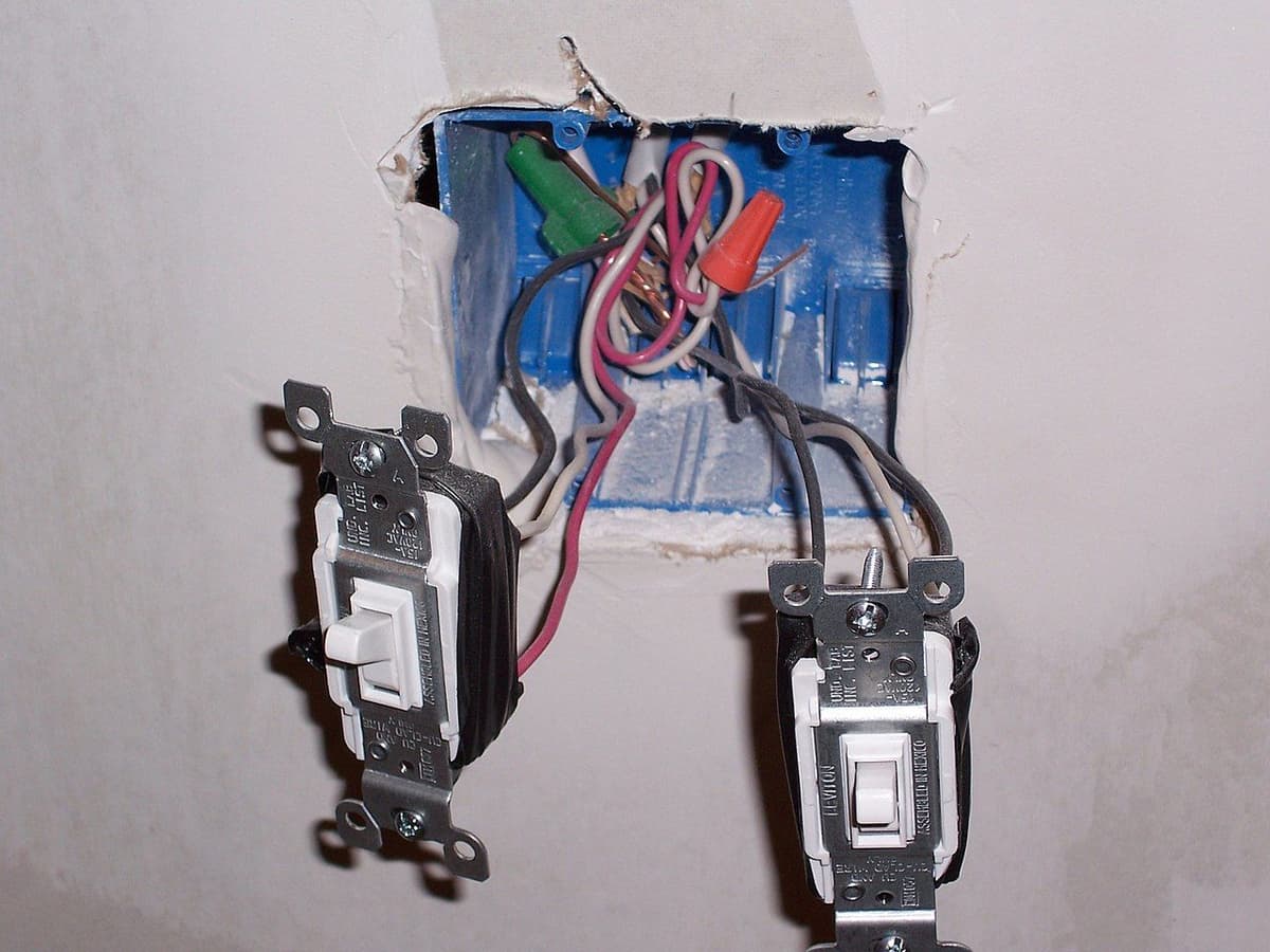 Doble interruptor de pared con el frontal retirado y los conductores visibles